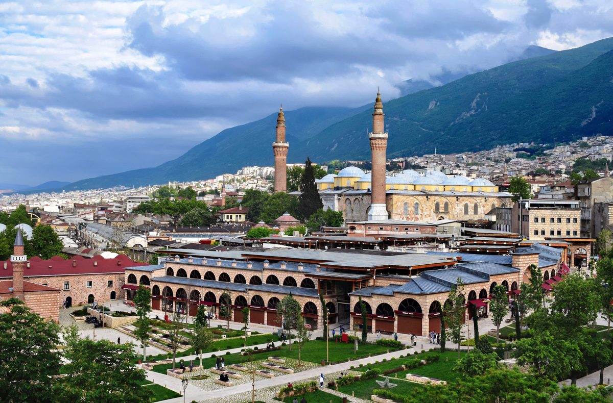 The domes and two minarets of the Ulu Cami in Bursa, with the arcaded old market buildings in front and the slopes of Uludağ behind