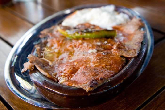 A plate of İskender kebab, thin slices of meat in tomato sauce with yogurt and a grilled pepper A plate of İskender kebab, thin slices of meat in tomato sauce with yogurt and a grilled pepper