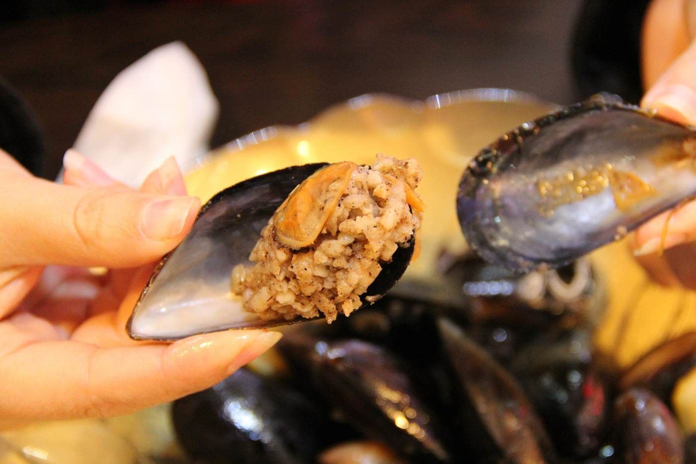 A stuffed mussel, midye dolma, held open in its shell to show the spiced rice inside