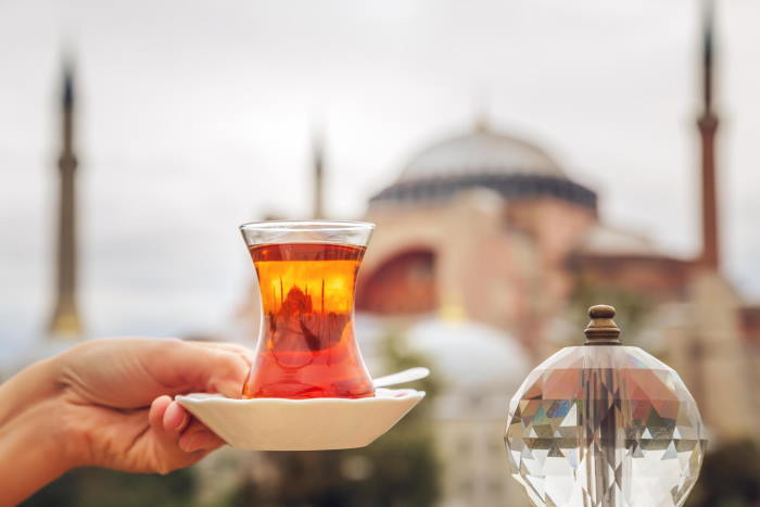 A tulip glass of Turkish tea held up in front of Hagia Sophia in Istanbul
